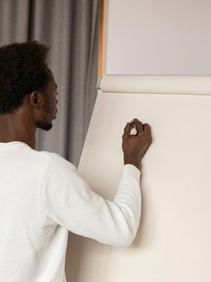 Back view of a man writing on a whiteboard during a presentation indoors.