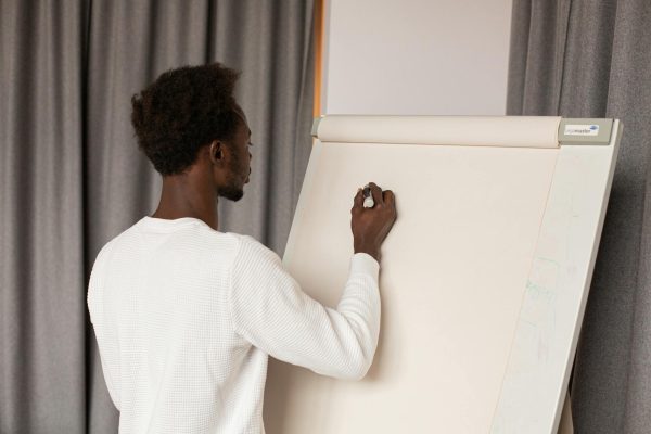 Back view of a man writing on a whiteboard during a presentation indoors.