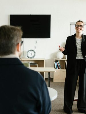 Businesswoman giving presentation in office with bookshelves and clock.