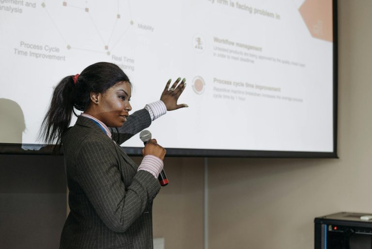 Businesswoman presenting with microphone, discussing improvements with a slide projection in a conference room.